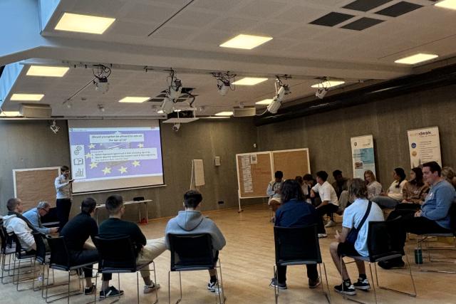 Die Teilnehmenden lauschen einem Referenten zum Thema Rhetorik und politische Argumentation. Im Hintergrun wird eine PowerPoint Präsentation präsentiert.